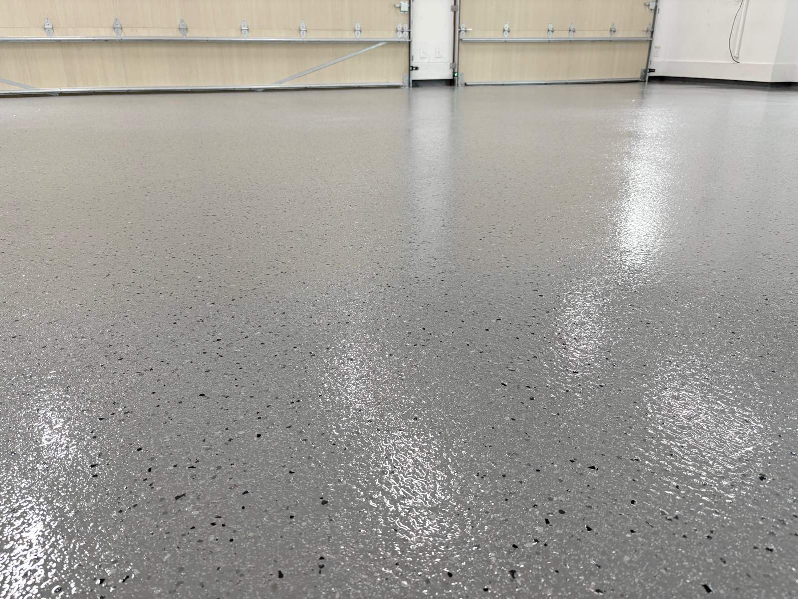 Finished full-flake garage floor coating in a grey and black blend, looking toward the garage door
