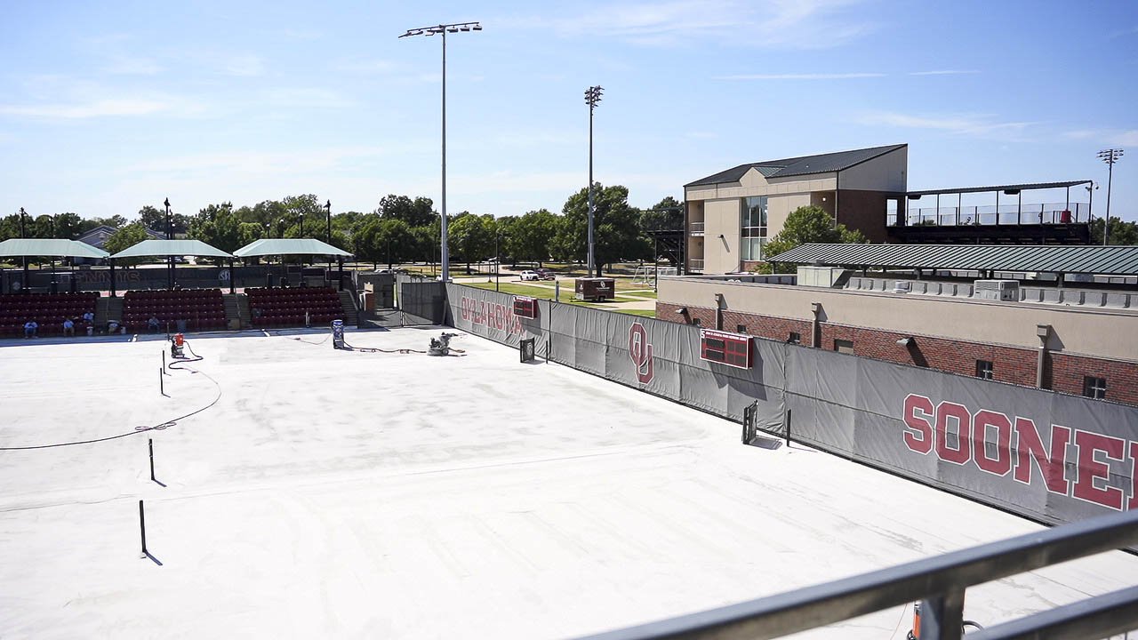 Outdoor courts at OU Headington with acrylic resurfacer going down before the color coats, grandstand and Sooners windscreen behind