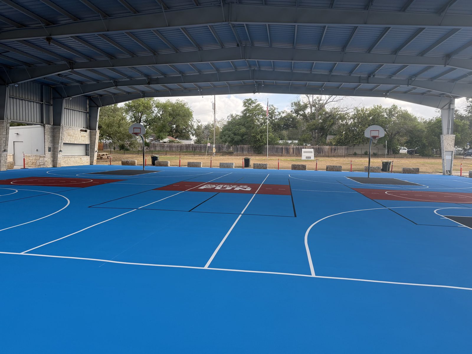 Outdoor basketball court with dark grey key and light blue field under a pavilion